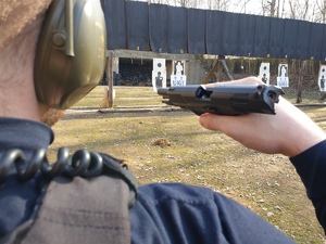 strzelnica zewnętrzna - policjant pokazuje pistolet z pustą komorą nabojową do sprawdzenia przez prowadzącego strzelanie