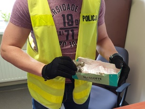 zdjęcie poglądowe z archiwum - policjant kryminalny trzyma pudełko z narkotykami w woreczkach