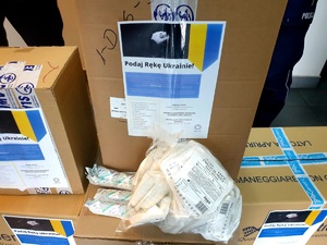 pudłach z zebranymi środkami, na każdym naklejona informacja z napisem podaj rękę Ukrainie, flagą Ukrainy i napisami, na jednym z pudeł worek przeźroczysty z środkami opartunkowymi
