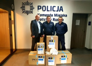 dwóch policjantów i przedstawiciel fundacji stoją przy pudłach z zebranymi środkami