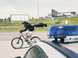 rowerzysta na ścieżce, w tle ulica, samochody, radiowóz