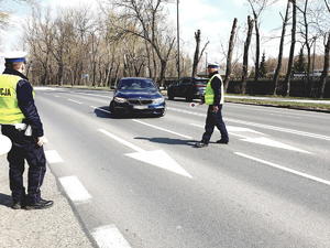 policjanci z drogówki, jeden z nich zatrzymuje do kontroli samochód koloru granatowego