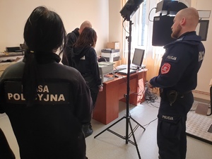 policjant i młoda kobieta patrzą jak technik skanuje odciski palców innej uczennicy