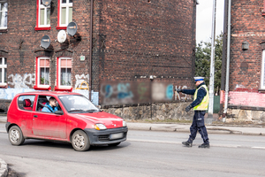 budynki, ulica, czerwony samochód zatrzymany przez policjanta z drogówki - zdjęcie poglądowe