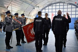 Hala gimnastyczna, stojący nowo przyjęci policjanci przed sztandarem w trakcie ślubowania
