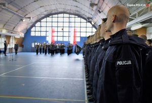 Hala gimnastyczna, stojący nowo przyjęci policjanci, w tle policjanci z orkiestry