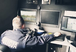 policjant z drogówki wewnątrz samochodu wyposażonego w sprzęt do monitoringu. na zdjęciu widać policjanta i monitory służące do podglądu z kamer