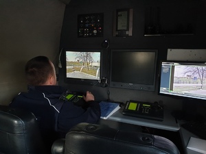 policjant z drogówki wewnątrz samochodu wyposażonego w sprzęt do monitoringu. na zdjęciu widać policjanta i monitory służące do podglądu z kamer