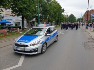 policyjna orkiestra idąca na czele pochodu ulicą, przed nimi policyjny radiowóz