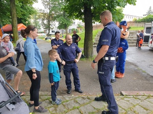 policjanci z maskotka na festynie, rozmawiają z chłopcem i jego mamą