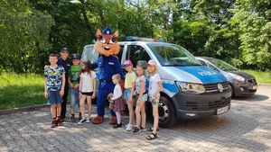 policjanta i dzieci pozują z maskotką na tle policyjnego radiowozu