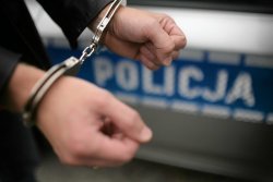 ręce w kajdankach, na tle policyjnego radiowozu