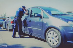 policjant zaglądający przez szybę do samochodu stojącego na parkingu - zdjęcie poglądowe