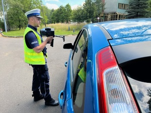 policjant z drogówki przy niebieskim samochodzie pokazuje kierowcy wynik pomiaru ze zdjęciem