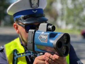 policjant z drogówki z laserowym miernikiem prędkości w trakcie pomiaru