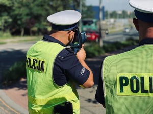 policjant z drogówki z laserowym miernikiem prędkości w trakcie pomiaru, obok stoi drugi policjant