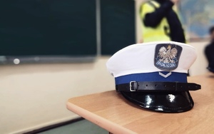 Policyjna czapka, a w tle policjant rozmawiający o bezpieczeństwie w ruchu drogowym