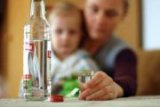 zdjęcie poglądowe, na stole stoi butelka wódki, kieliszek w tle matka z dzieckiem na kolanach
