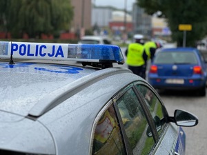 ulica w centrum miasta, stojący radiowóz i przed nim niebieski samochód przy którym stoją dwaj policjanci