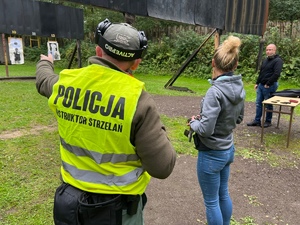 zajęcia strzeleckie na strzelnicy otwartej, instruktor omawia kolejne zadanie strzeleckie, w tle kobieta i mężczyzna po cywilu