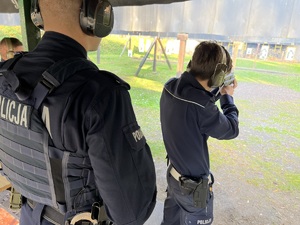strzelnica otwarta - policjant drogówki strzela z pistoletu maszynowego, za nim stoi umundurowany policyjny instruktor