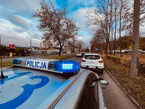 droga, radiowóz, zaparkowane samochody na pasie ruchu przy cmentarzu