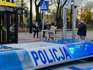 radiowóz, autobus, przejście dla pieszych, piesi i policjant stojący na przejściu