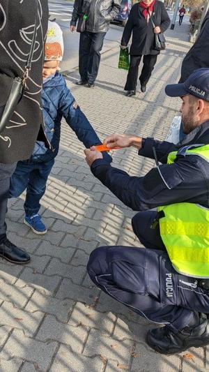 chodnik przed cmentarzem, dzielnicowy zakłada opaskę na rękę dziecka