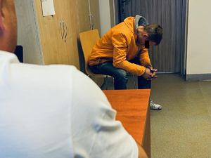 zatrzymany mężczyzna siedzi na krześle w pokoju biurowym, na pierwszym planie plecy policjanta po cywilu