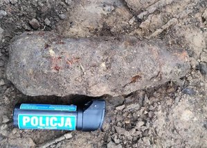 niewypał lezący w ziemi, obok policyjny gaz łzawiący dla pokazania wielkości