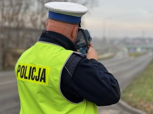 zdjęcie przedstawia policjanta w mundurze sprawdzającego prędkość pojazdów przy pomocy radarowego miernika prędkości