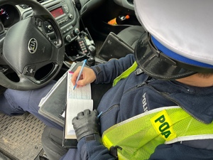 zdjęcie przedstawia policjanta w radiowozie wypisującego mandat karny