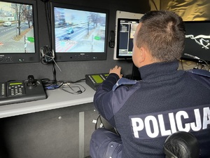 zdjęcie przedstawia policjanta wewnątrz samochodu mobilnego stanowiska monitoringu, z tyłu widać monitory z obrazem z kamer