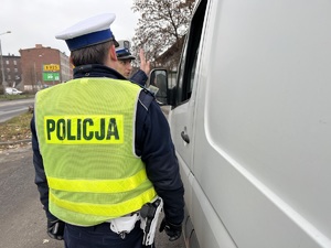 zdjęcie przedstawia dwóch policjantów stojących przy białym samochodzie dostawczym rozmawiających z jego kierowcą