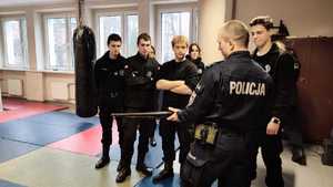 zdjęcie przedstawia uczniów klasy policyjnej gdy policyjny instruktor prezentował im broń używaną przez policjantów