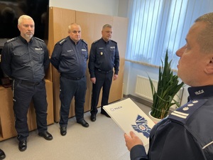 zdjęcie przedstawiające pożegnanie odchodzących na emeryturę dyżurnych - policjanci stojący, komendant składa gratulacje