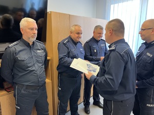 zdjęcie przedstawiające pożegnanie odchodzących na emeryturę dyżurnych - policjanci stojący, komendant i zastępca gratulują