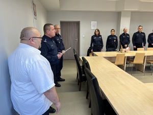 zdjęcie przedstawiające pożegnanie odchodzącego na emeryturę komendanta komisariatu- policjanci stojący, komendant i zastępca, naczelnicy na sali odpraw