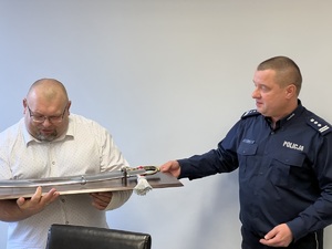 zdjęcie przedstawiające pożegnanie odchodzącego na emeryturę - komendant przekazuje okolicznościowy prezent pamiątkowy - szabla na drewnie