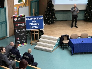 zdjęcie przedstawia, aulę szkoły na scenie przemawia kierowca rajdowy, przed nią siedzą policjanci