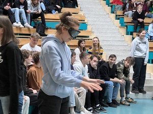 zdjęcie przedstawia uczennicę w narkogoglach próbującą przejść tor przeszkód, z tyłu widać siedzących uczniów