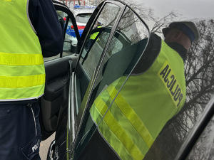 zdjęcie przedstawia policjanta drogówki przy samochodzie zatrzymanym do kontroli