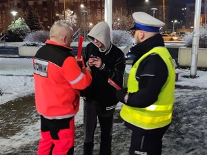 policjant i ratownik daje odblaskowe opaski młodemu mężczyźnie