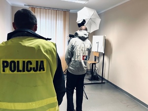 zdjęcie przedstawia pomieszczenie technika kryminalistyki i daktyloskopii, policjant z zatrzymanym czeka na wykonanie zdjęć