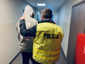 zdjęcie przedstawia korytarz komendy, policjant idzie z zatrzymanym