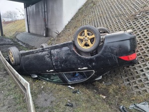 zdjęcie przedstawiające miejsce zdarzenia drogowego, leżący na dachu czarny samochód