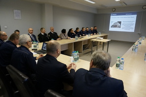 zdjęcie - sala odpraw, policjanci i goście siedzą przy stołach ustawionych w podkowę, na ścianie wyświetlany jest slajd prezentacji