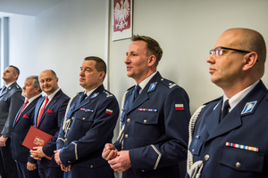 zdjęcie z sali odpraw przedstawia sześciu mężczyzn stojących w rzędzie, naczelnik prewencji, przewodniczący rady miejskiej, odchodzący komendant, nowy komendant i zastępca komendanta