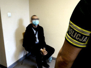 zdjęcie poglądowe, policjant stoi przy siedzącym mężczyźnie z maseczką na twarzy