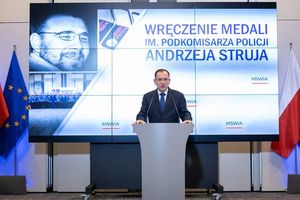 minister na tle telebimu ze zdjęciem poległego policjanta